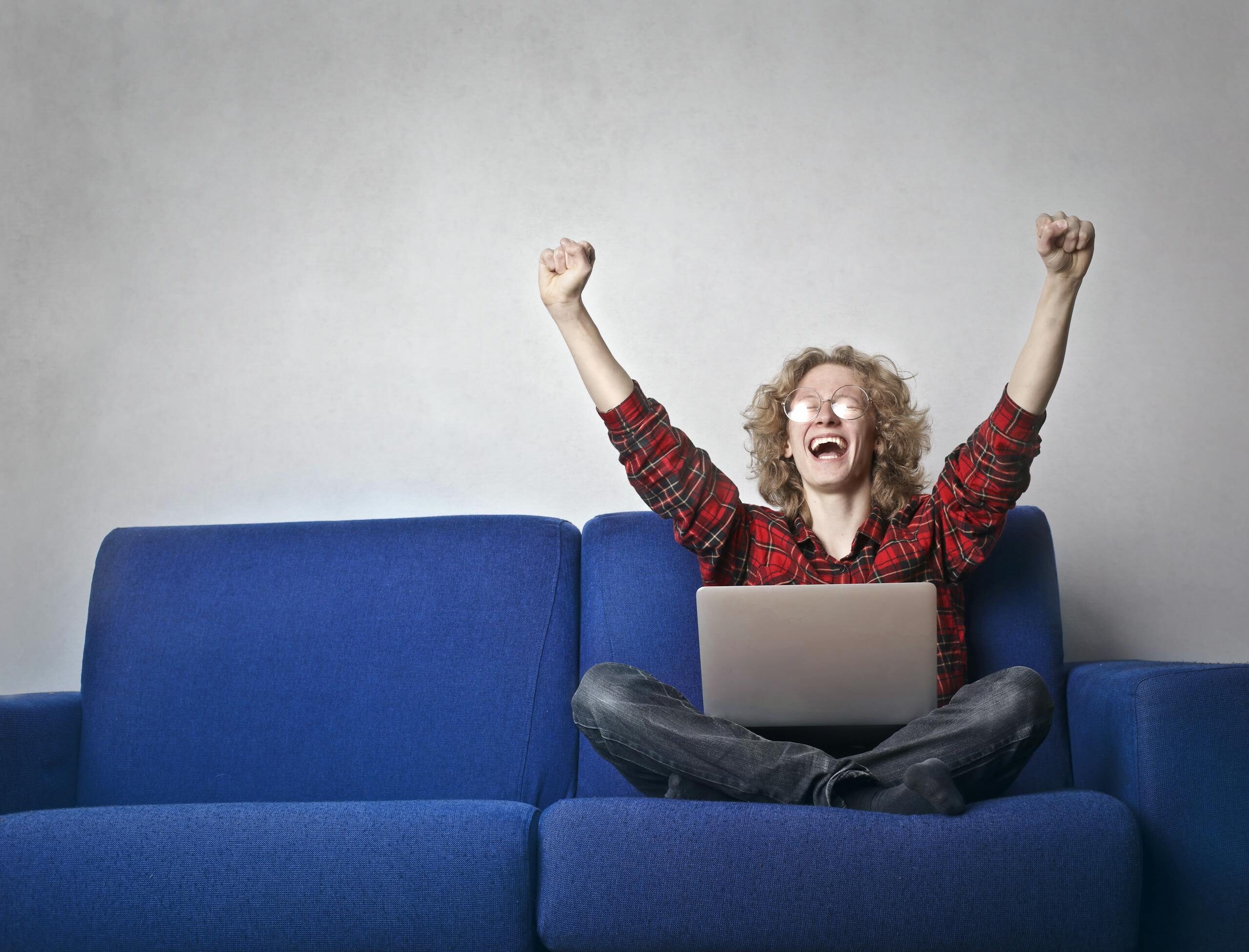 Obrazek przedstawiający rezultat wykonanej usługi sprzątania biur Thrilled individual celebrating success while using a laptop on a blue sofa indoors.